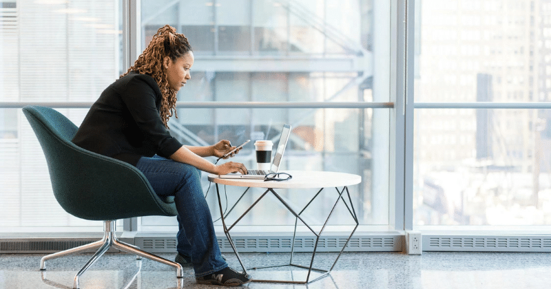 a woman sitting at a table with a laptop and a phone